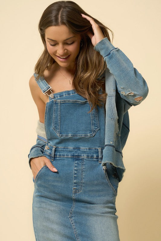 Close-up of denim blue skirt overalls: bib pocket, seams, and adjustable strap hardware