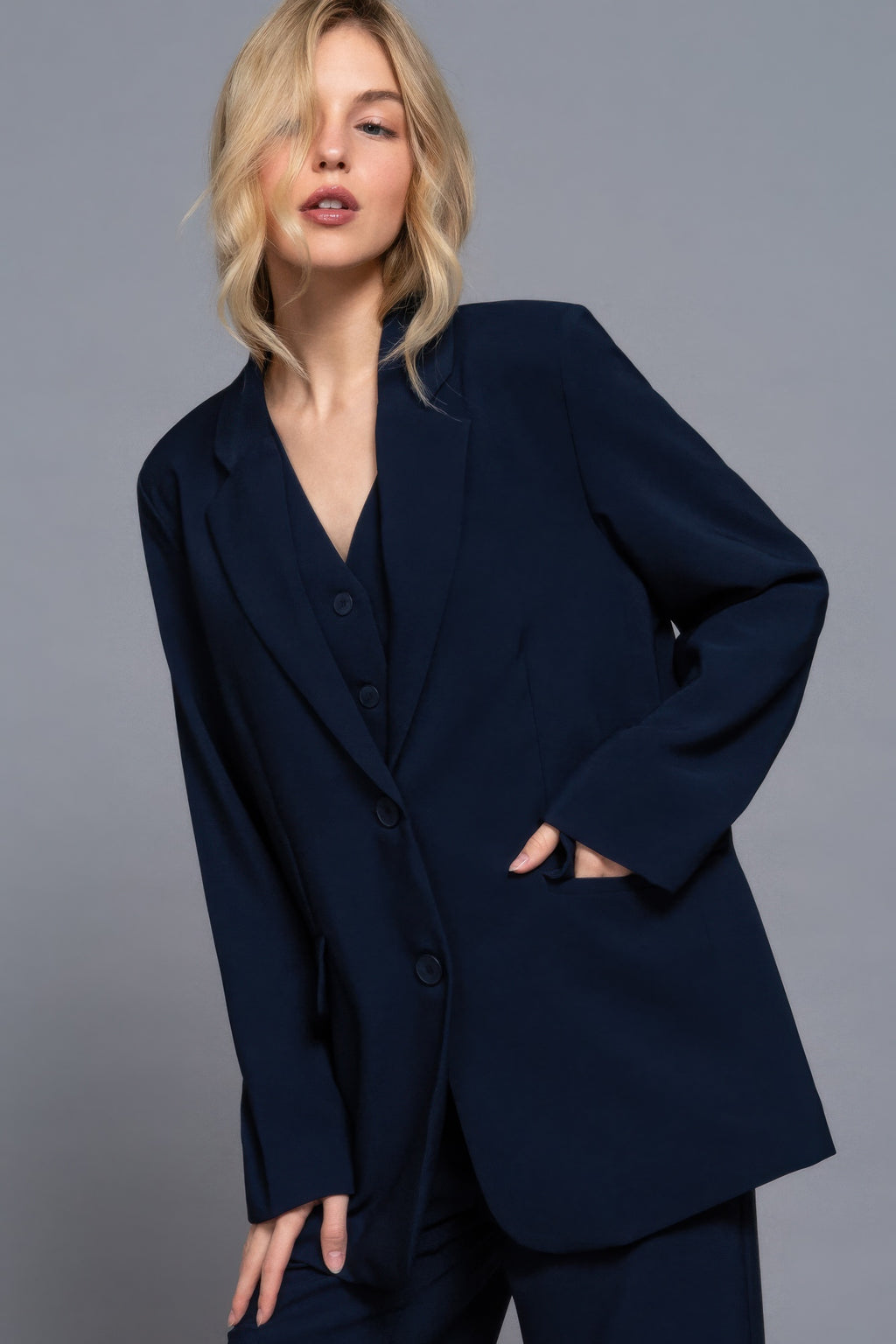 Long-sleeve navy blazer with V-neck, front buttons, and side pockets; relaxed fit.