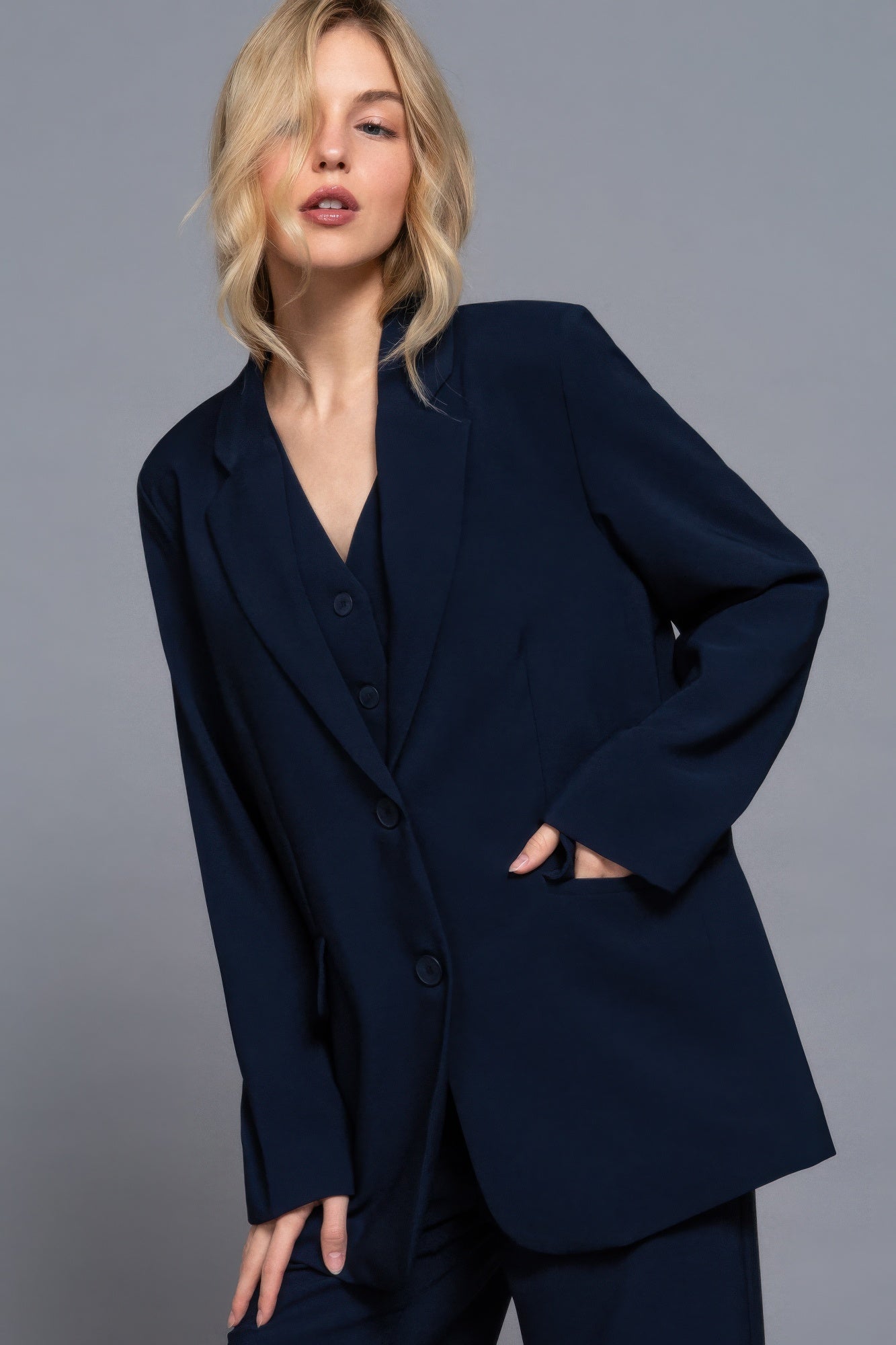 Long-sleeve navy blazer with V-neck, front buttons, and side pockets; relaxed fit.