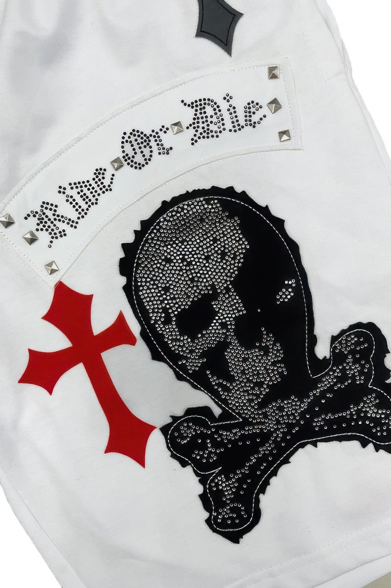 White shorts close-up: rhinestone skull face, small studs and cross patches