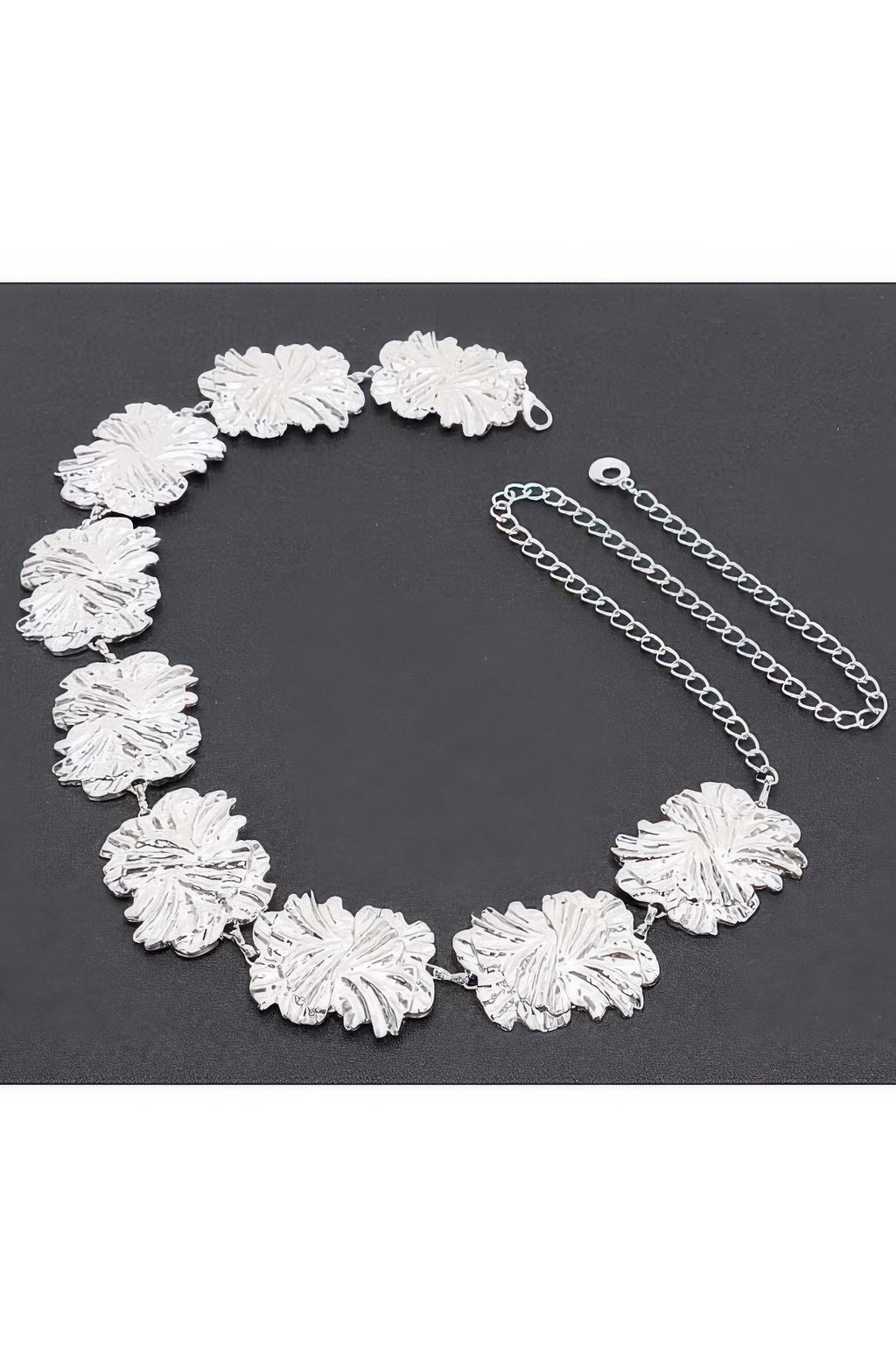 Silver metal chain belt laid flat, textured flower medallions with chain extender