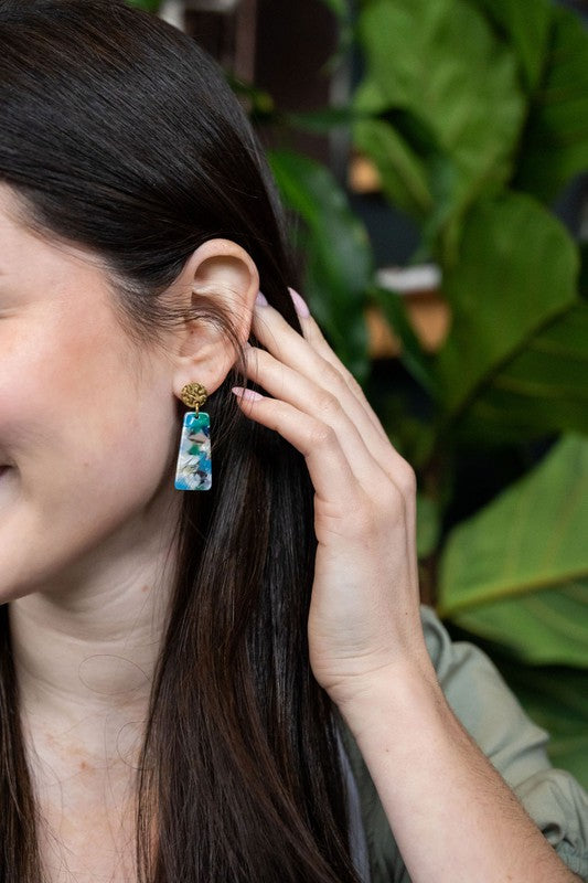 Mini resin drop earrings on ear: gold stud tops with blue, green and pink details