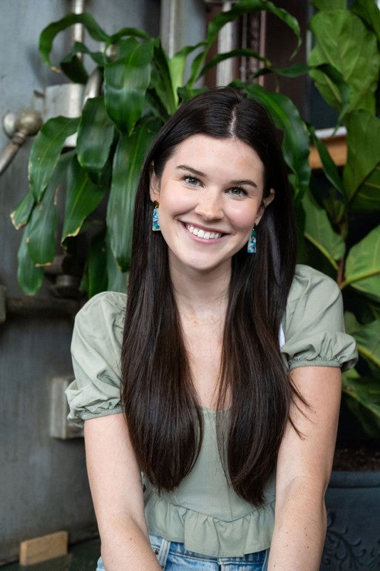 Earrings worn with long hair: gold stud tops and blue-green resin rectangle drops