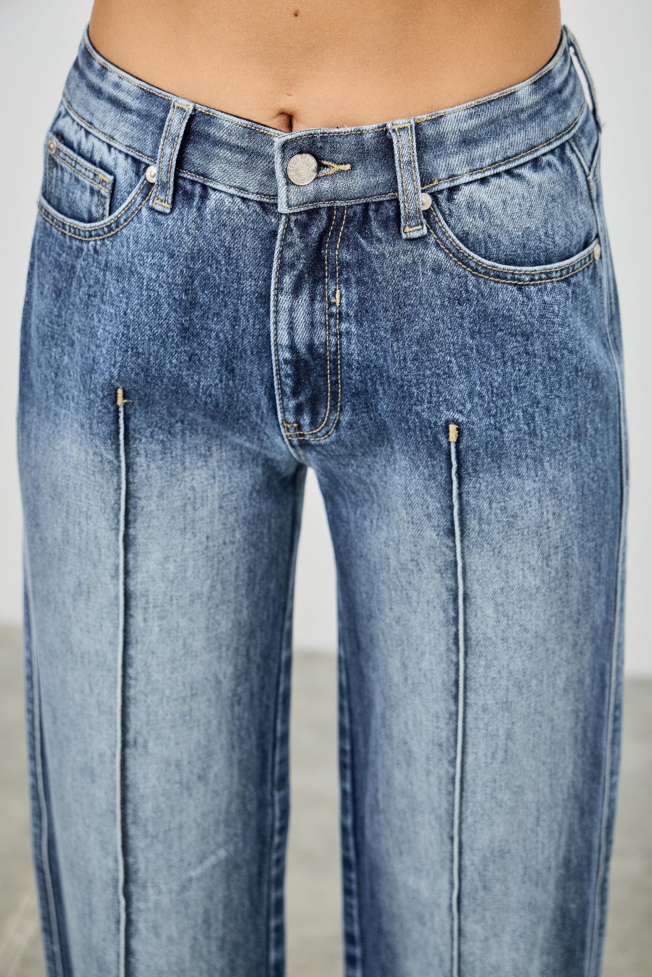 Waistband closeup: mid-rise straight jeans with pintuck seams, light blue denim, button