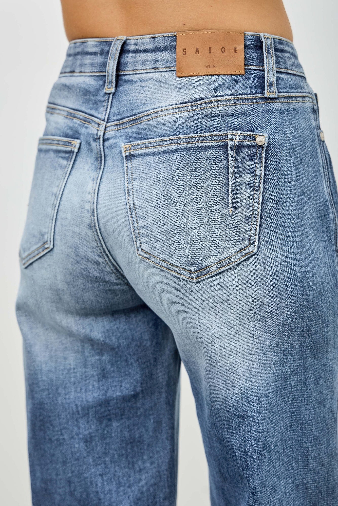 Back waistband close-up with leather brand patch and patch pocket, blue denim