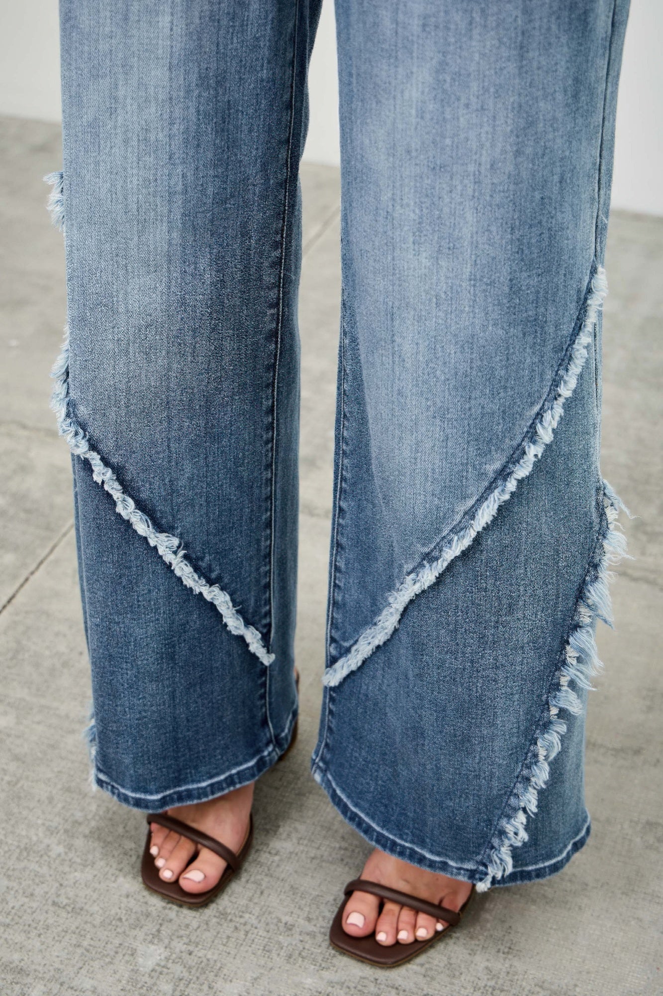 Close-up of wide-leg denim with diagonal frayed seam and raw hem edges