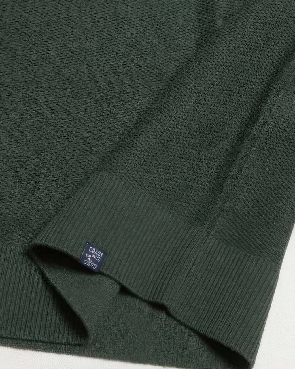 Dark green knit sweater sleeve cuff with ribbed hem and size tag