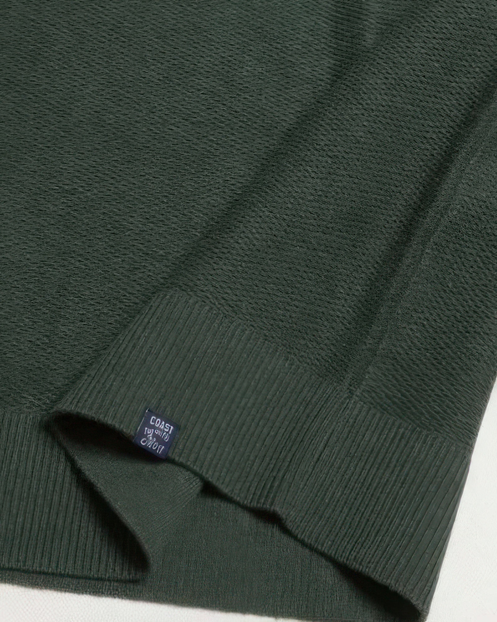Dark green knit sweater sleeve cuff with ribbed hem and size tag