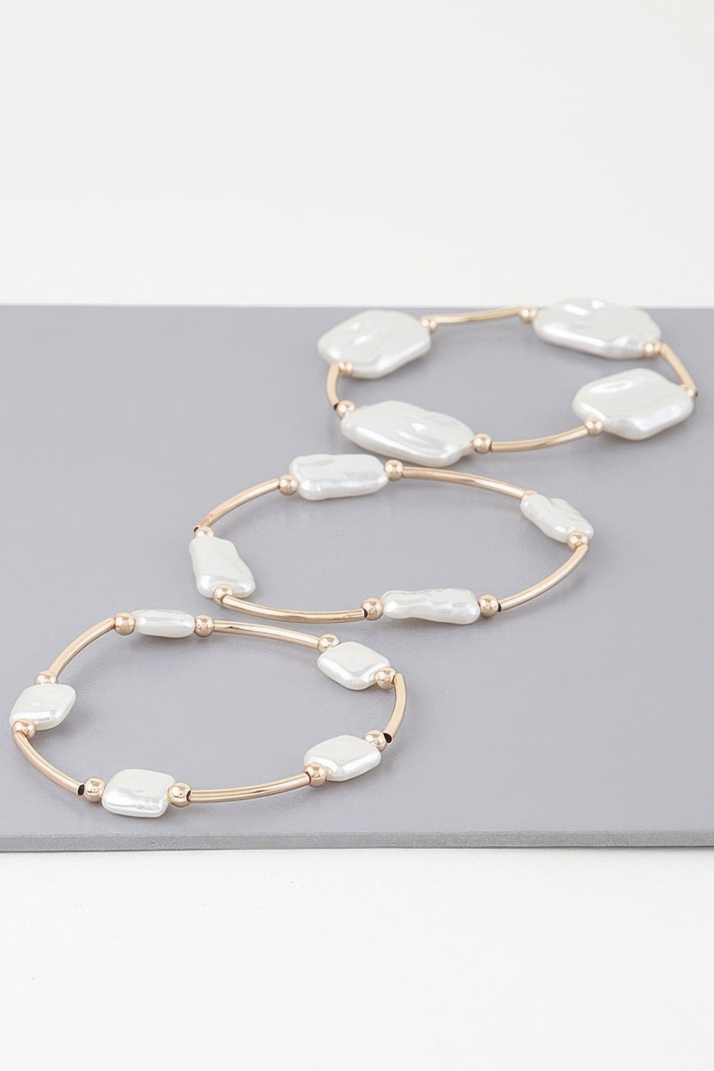 Three gold-tone pearl tube bracelets with white baroque stones in curved loops