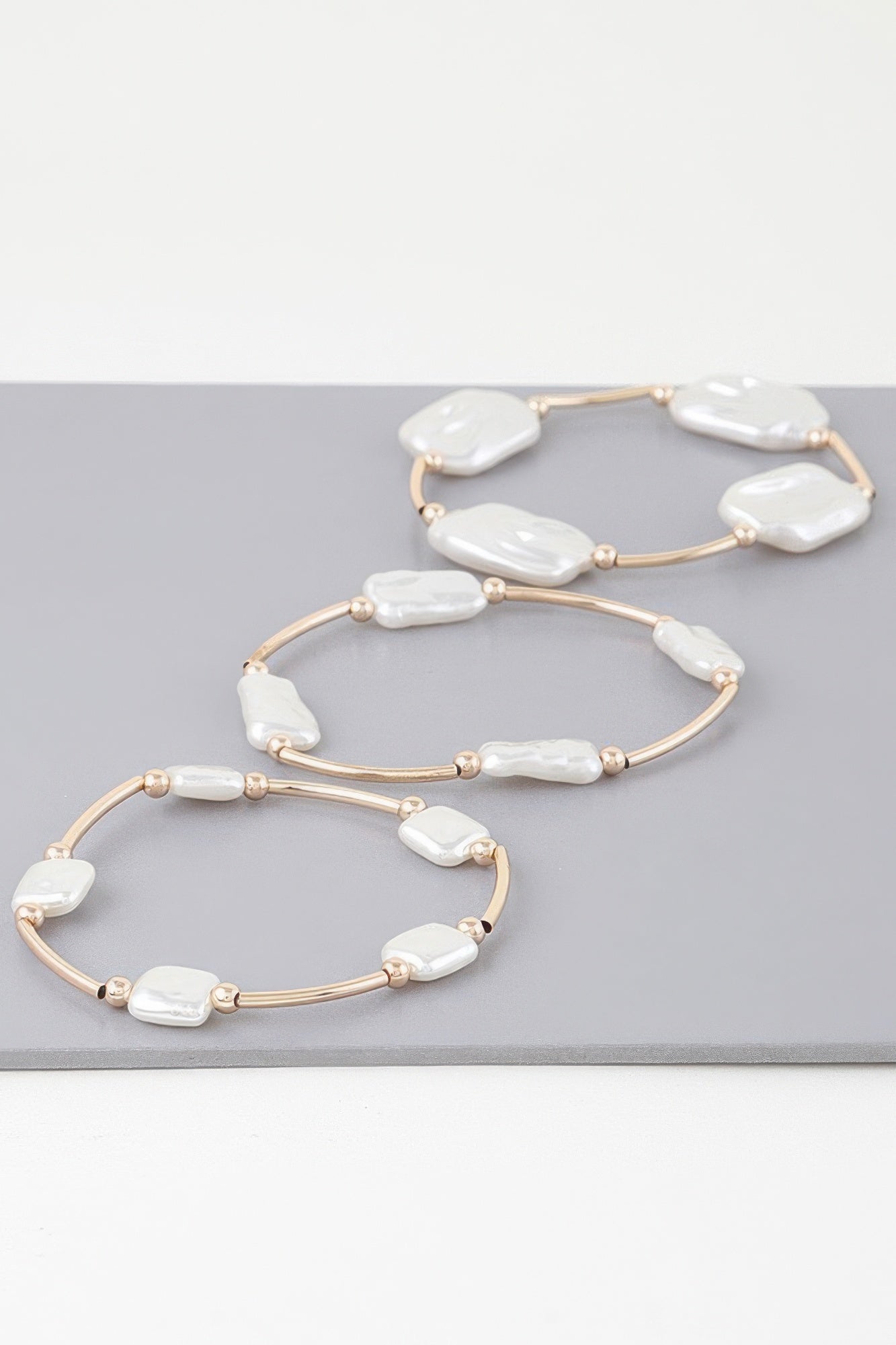 Three gold-tone pearl tube bracelets with white baroque stones in curved loops