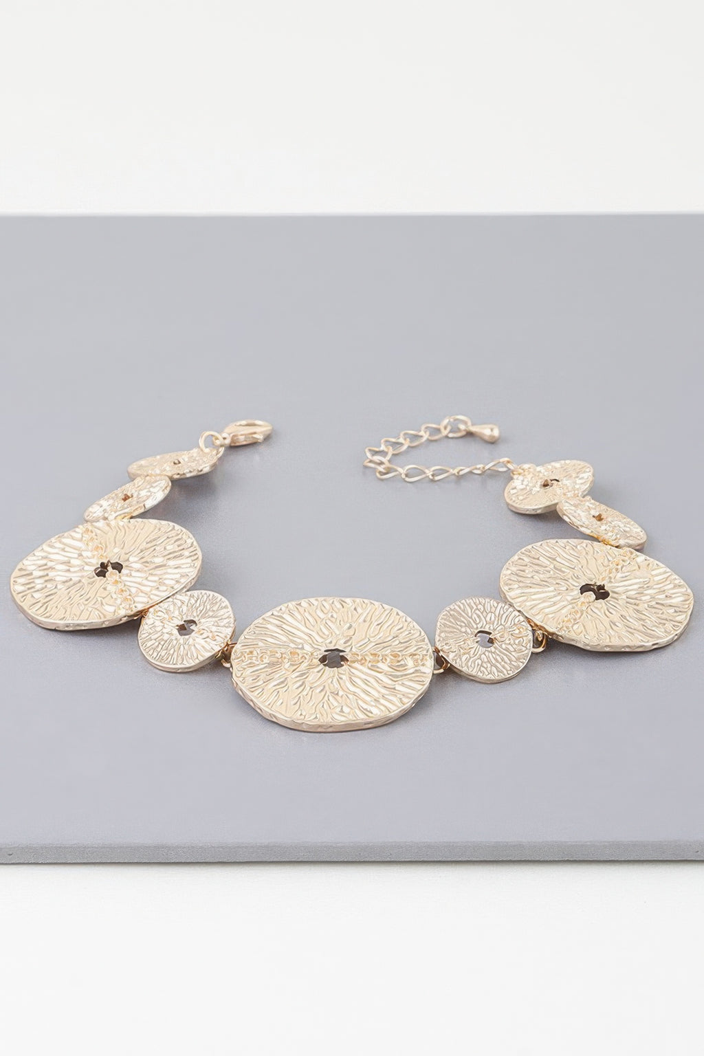Gold bracelet featuring hammered round discs linked by a chain, with round clasp
