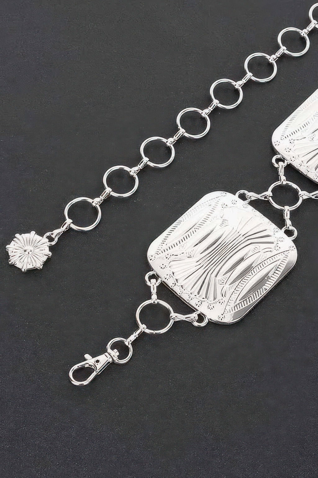 Close-up silver chain belt with engraved rectangular plate and oval ring links