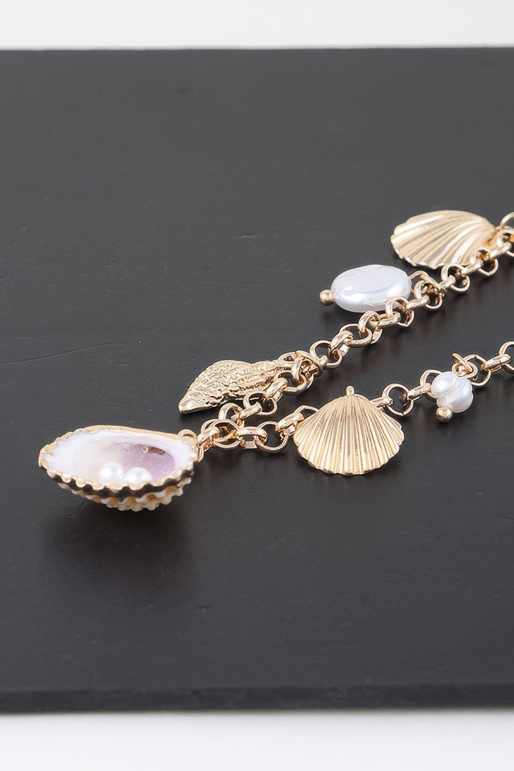 Close-up of gold chain necklace charms: scallop shell, fan shell, and white pearls