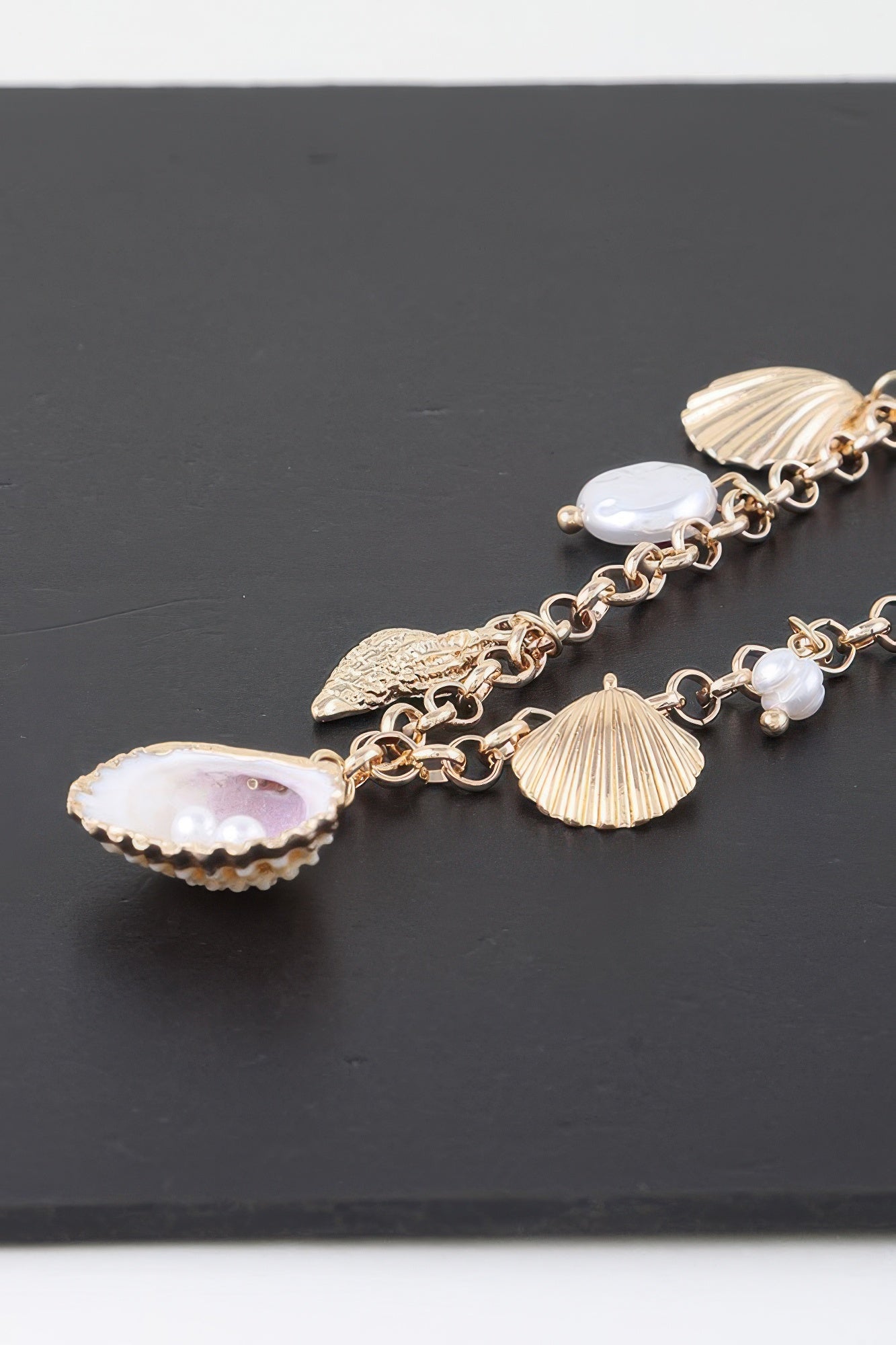 Close-up of gold chain necklace charms: scallop shell, fan shell, and white pearls