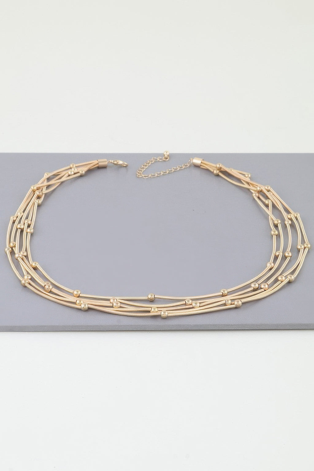 Multi pillar beaded necklace in gold tone, layered strands and bead details with clasp
