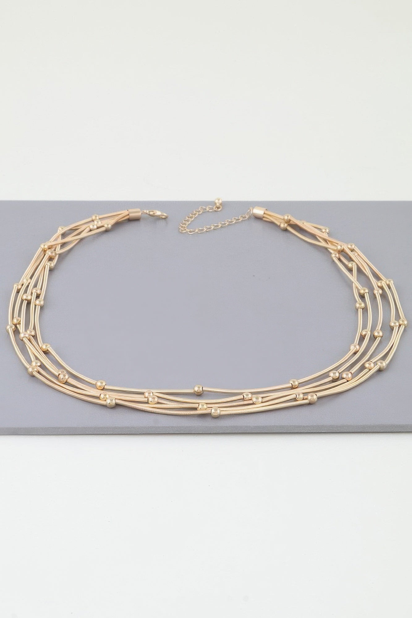 Multi pillar beaded necklace in gold tone, layered strands and bead details with clasp