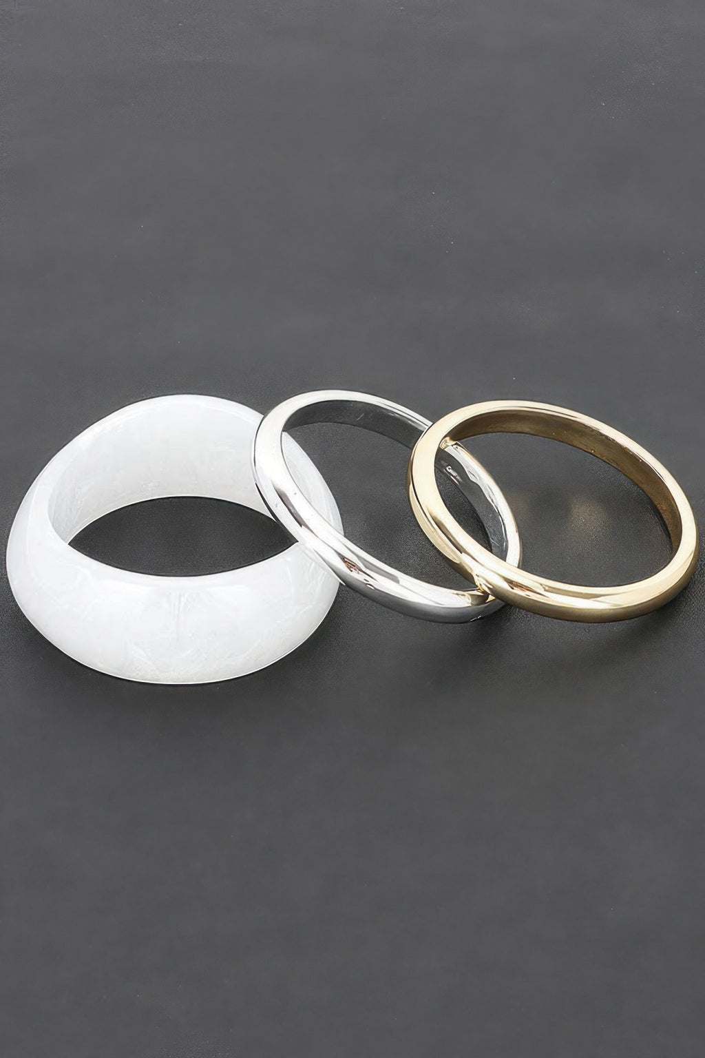 Drei Armreifen: weißer, silberner und goldfarbener Bangle mit polierter Oberfläche
