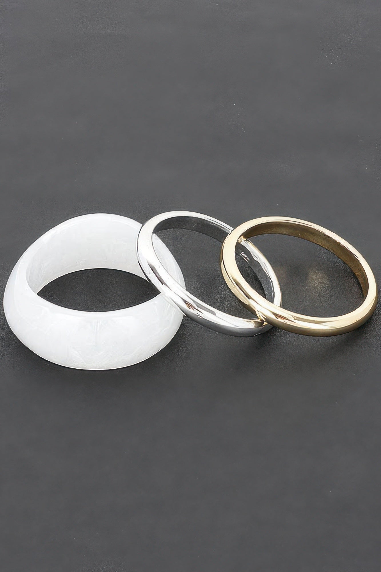 Drei Armreifen: weißer, silberner und goldfarbener Bangle mit polierter Oberfläche
