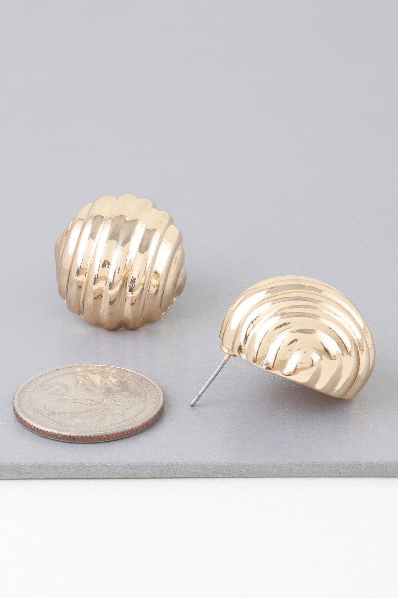 Gold dome ribbed stud earring with post, beside coin for size
