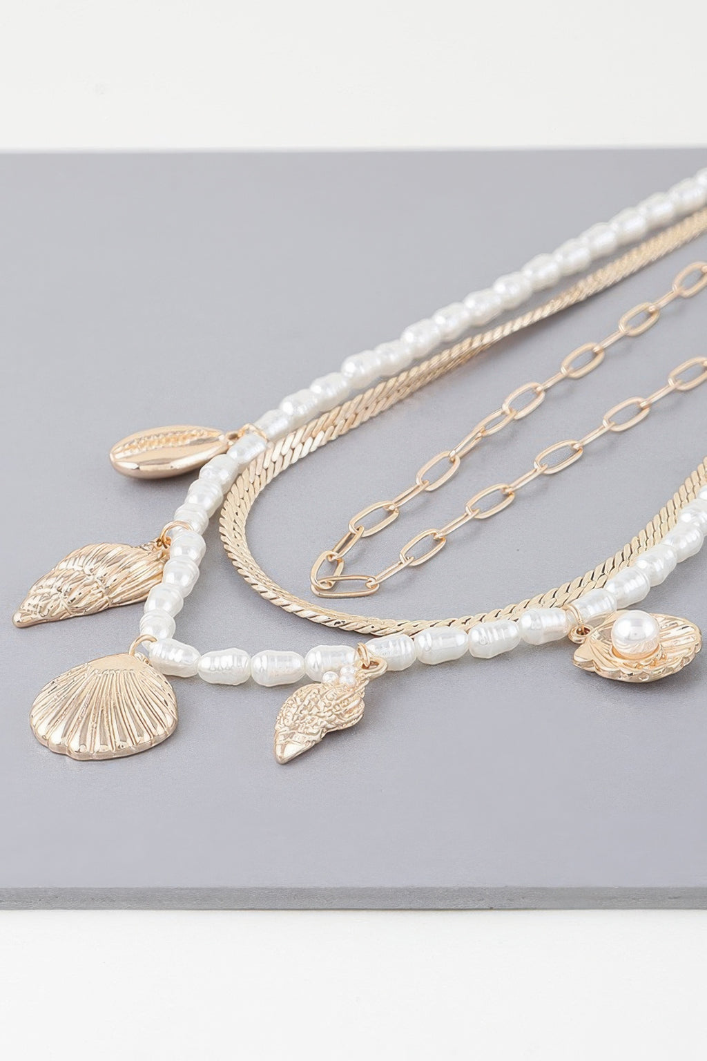 Layered chains close-up: white bead strand, gold seashell charms, and small pearls