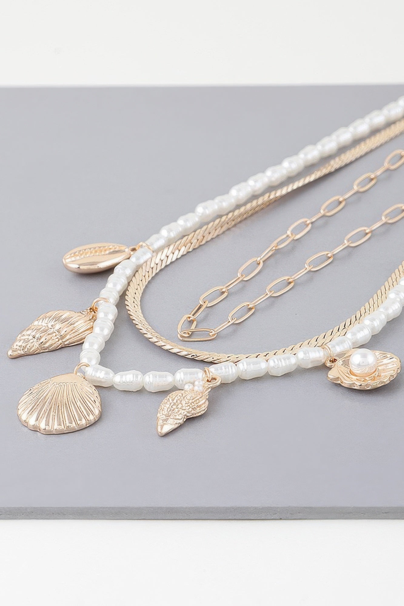 Layered chains close-up: white bead strand, gold seashell charms, and small pearls