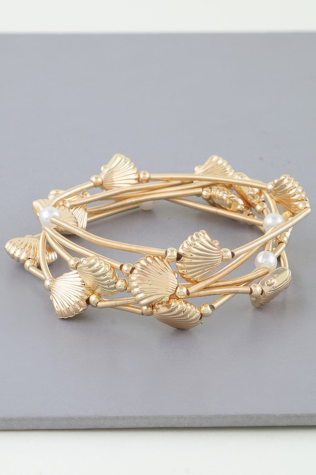 Gold multi-row coil bracelet with seashell charms and small pearl accents