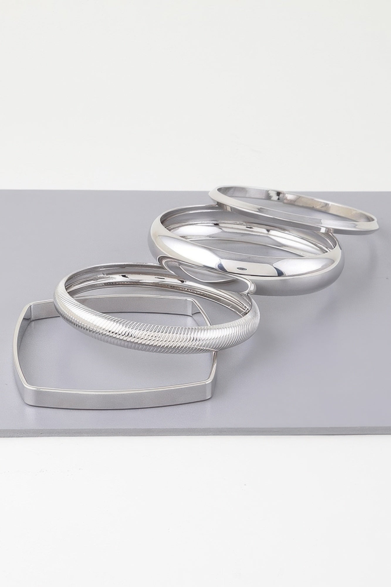Silver layered bangles on rectangular display: ridged cuff and polished rings