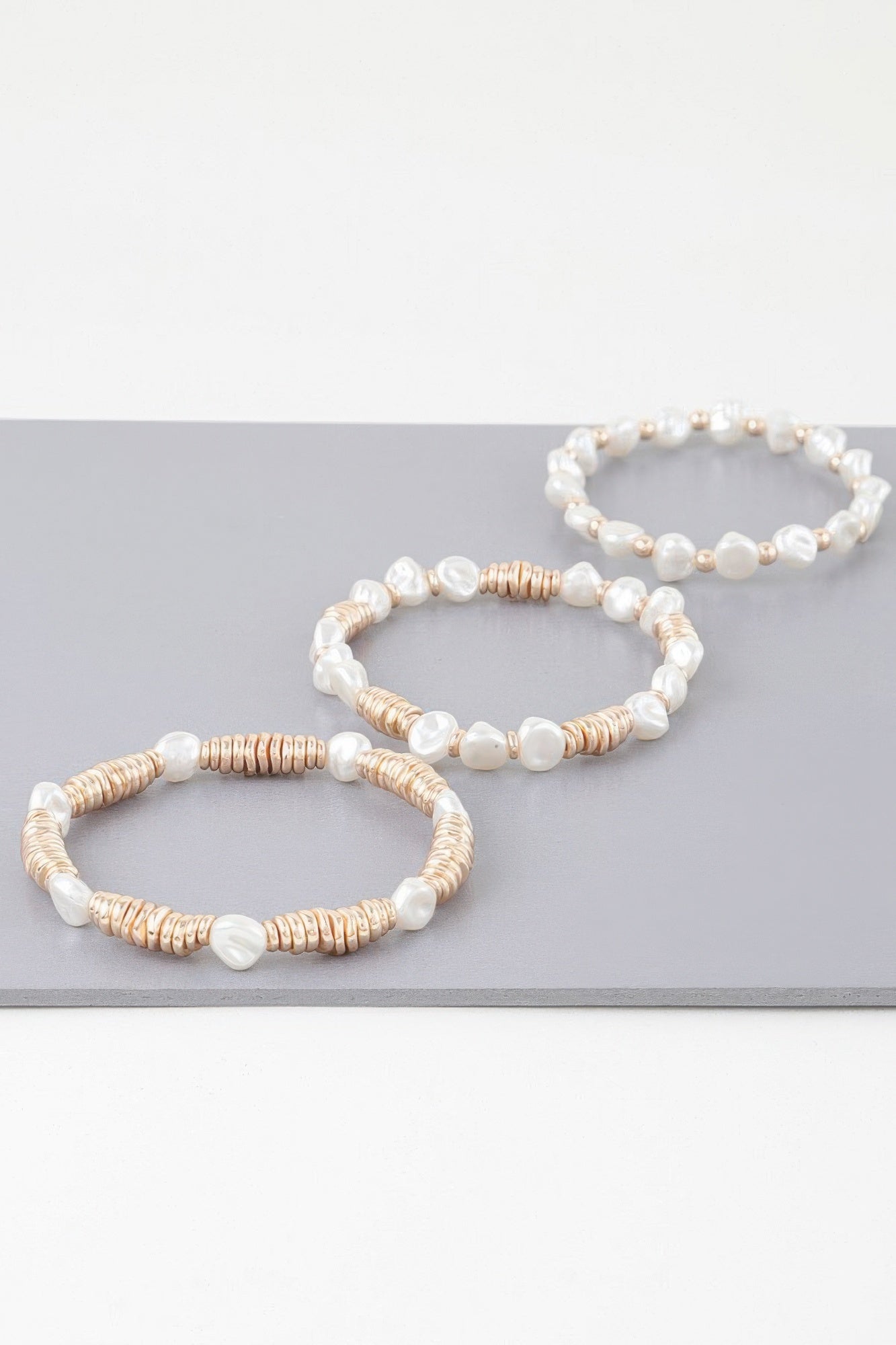 Three individual bracelets with white pearl beads and gold-toned heishi-style spacers
