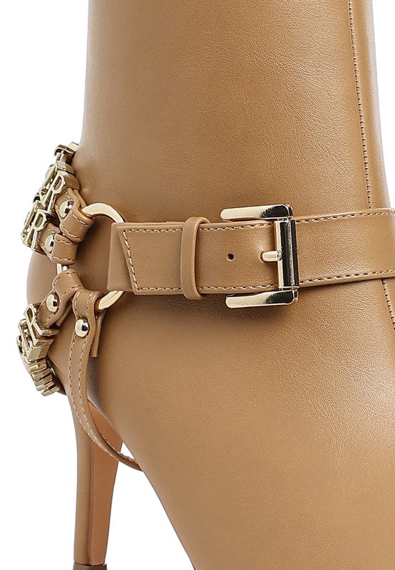 Tan harness ankle boot close-up with front strap, metal buckle, and chain-like accents