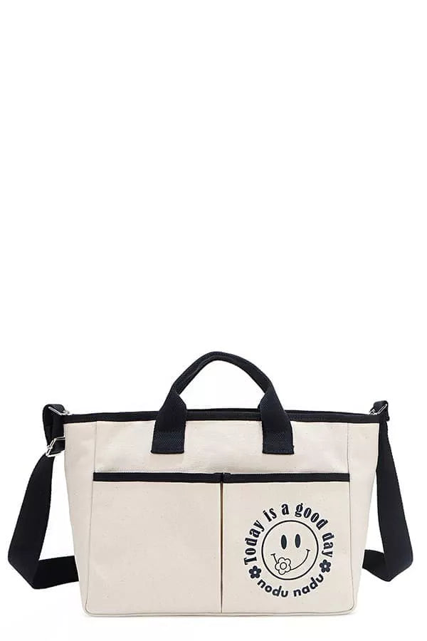 Beige canvas tote bag with navy handles, crossbody strap, and smiley logo front