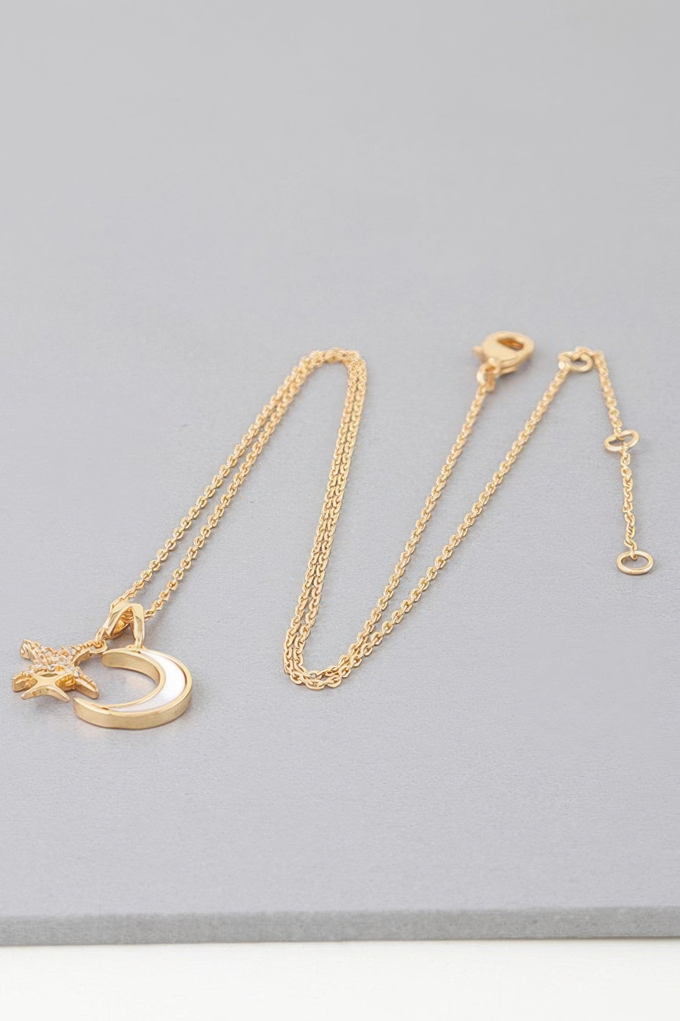 Gold moon-and-star pendant necklace with chain laid out