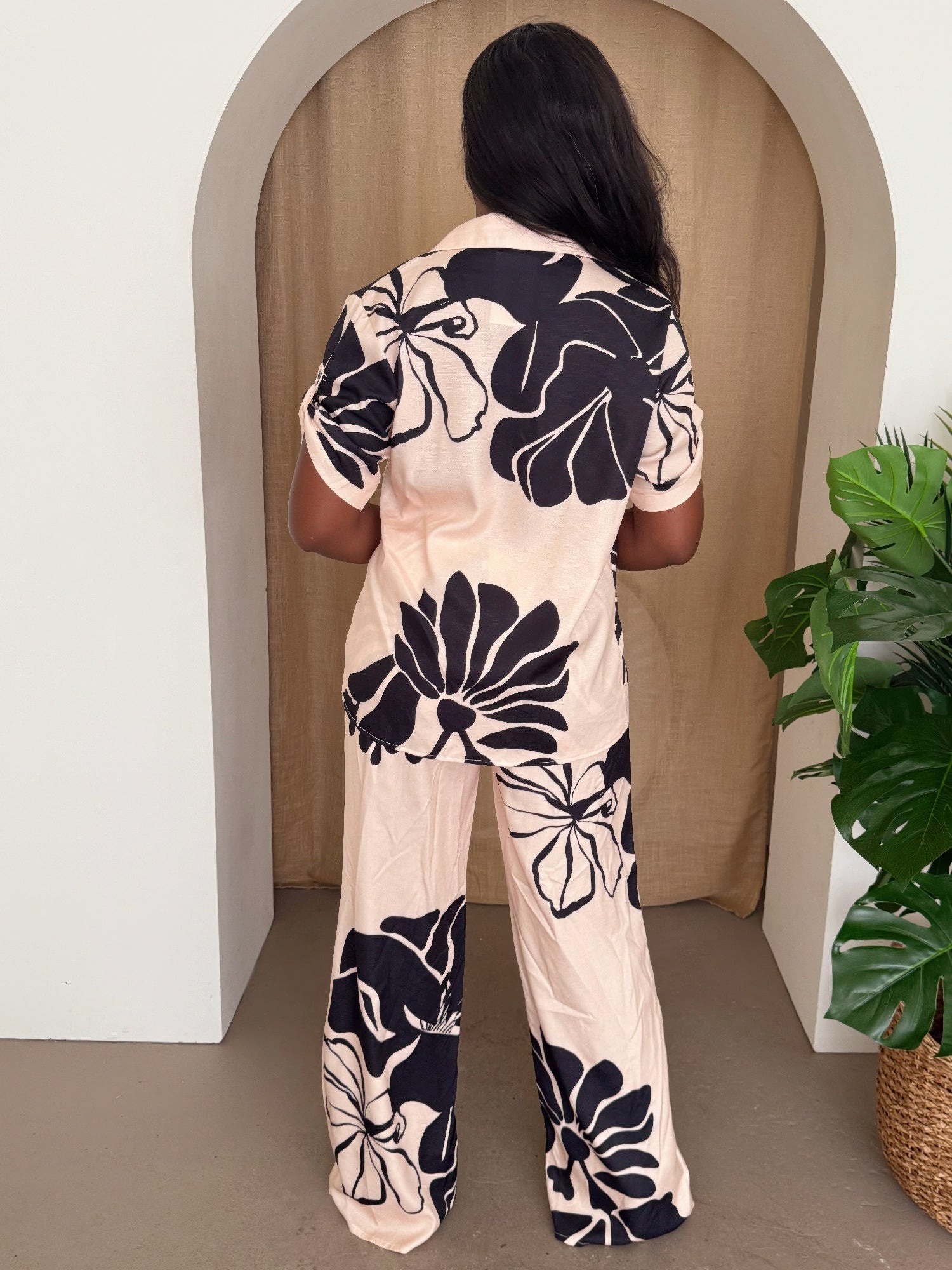 Back view: cream pants set with black floral print, short-sleeve button-up top and wide legs