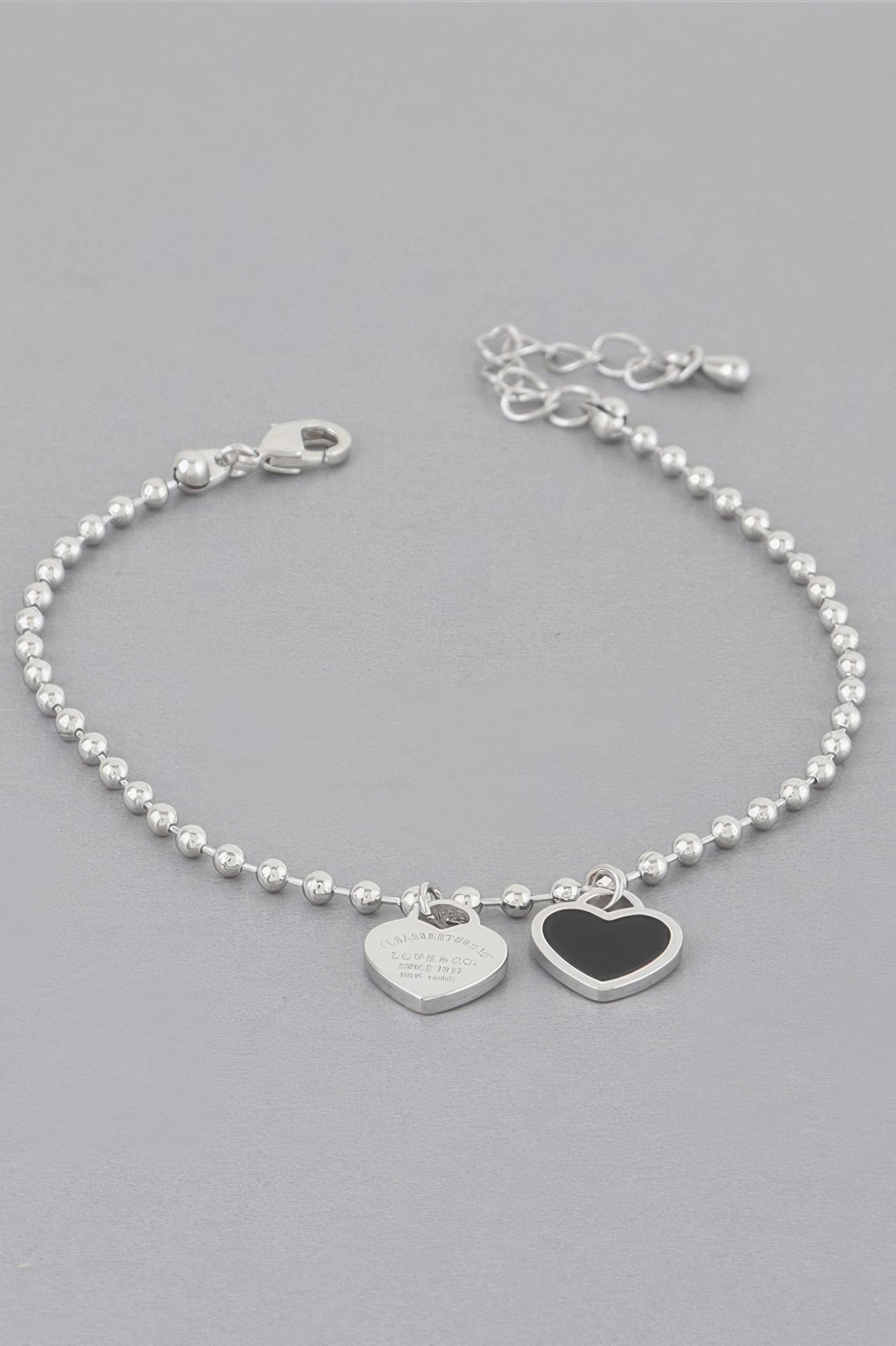 Love bracelet mit silberner Perlenkette und zwei Herzanhängern, davon einer dunkel umrandet