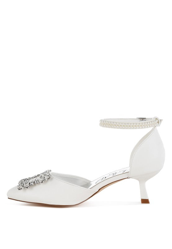 White kitten heel sandals with rhinestone brooch strap across the toe