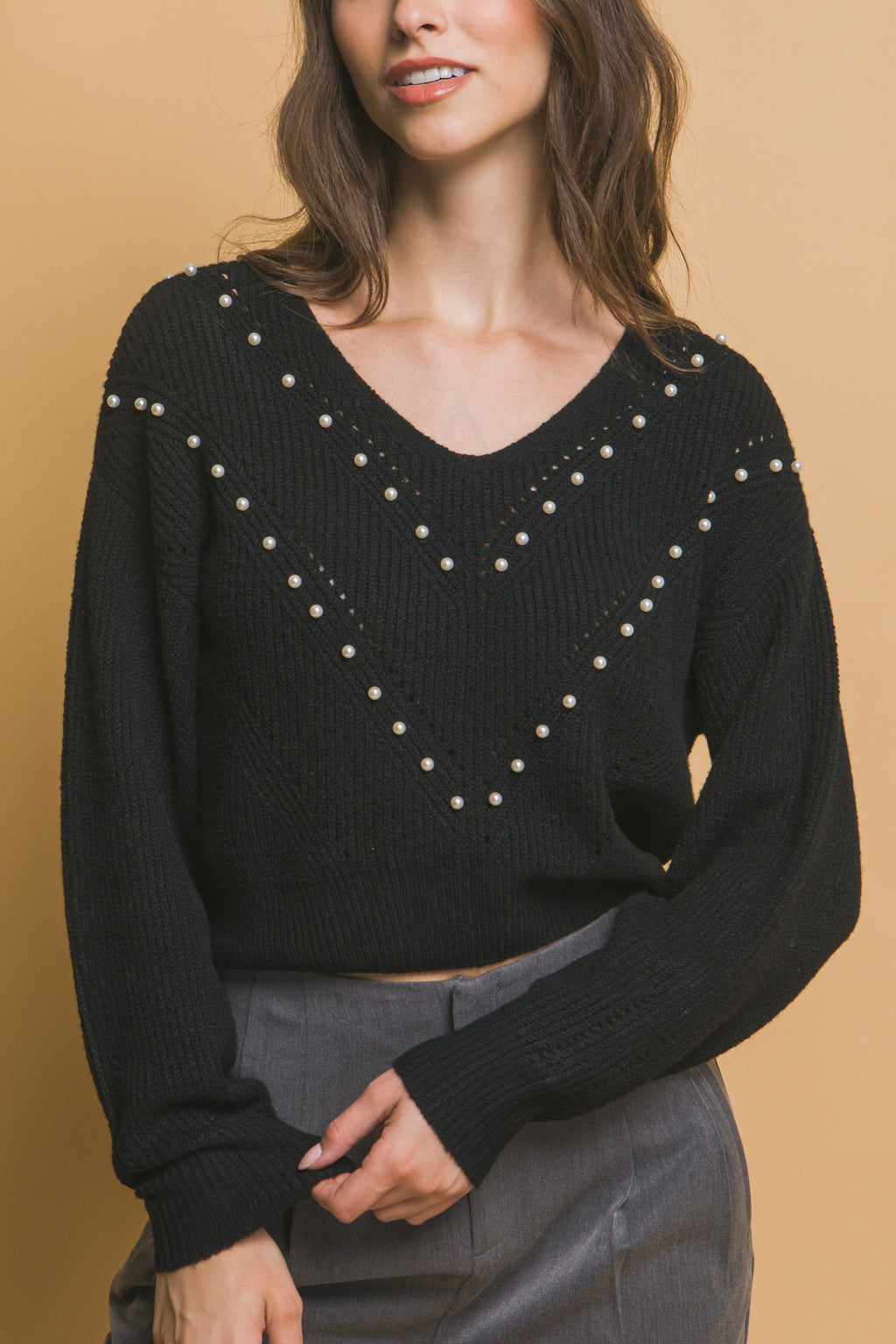 Black pearl-embellished V-neck knit sweater with long sleeves, hand on waist