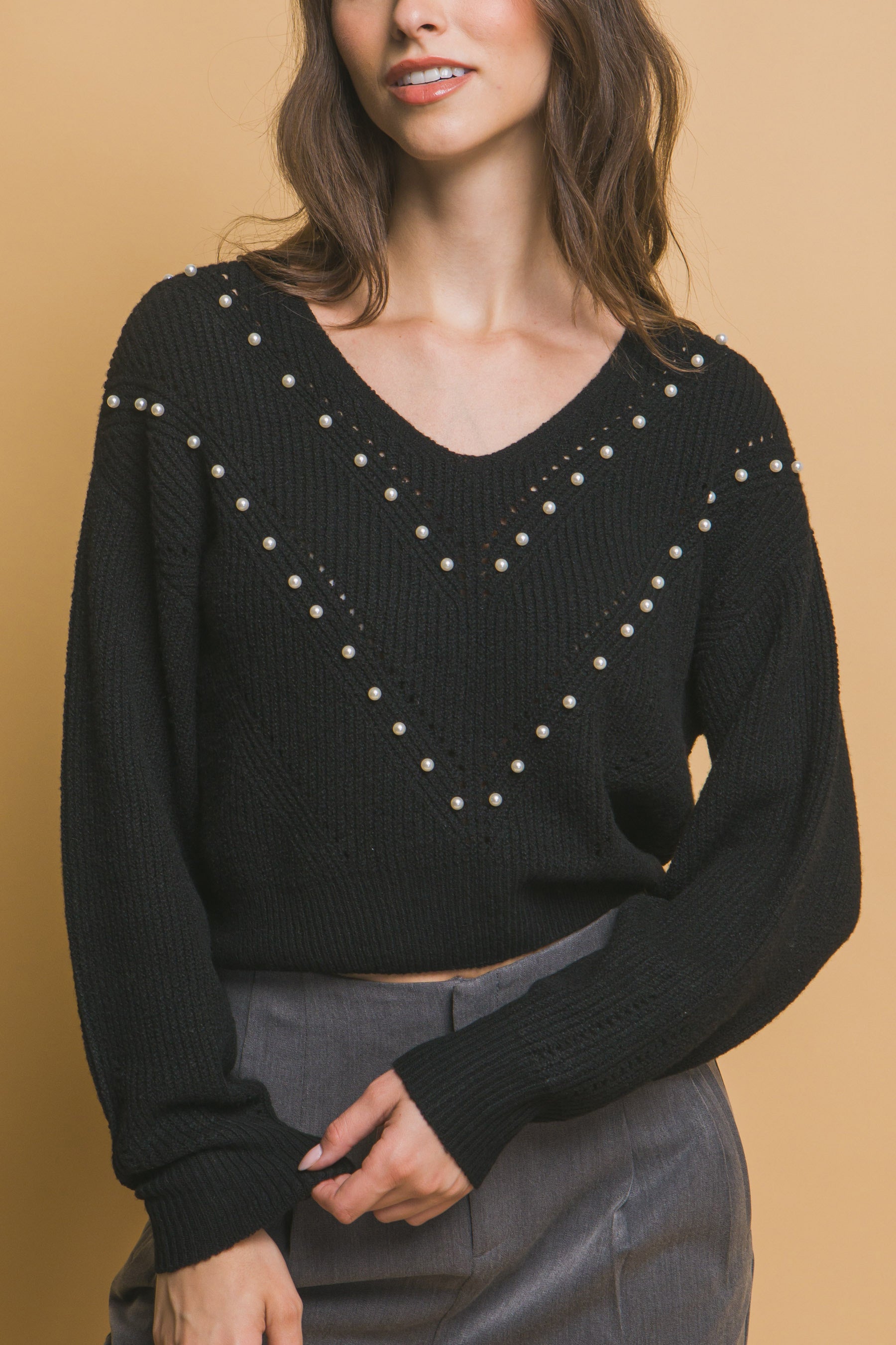 Black pearl-embellished V-neck knit sweater with long sleeves, hand on waist