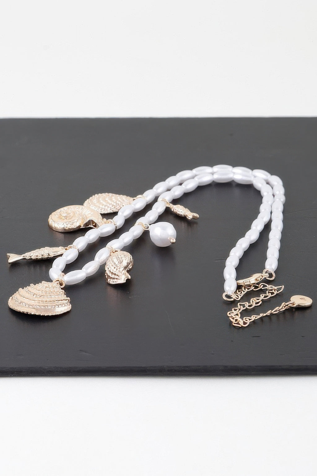 Under The Sea charm necklace laid flat: white beads with gold fish, shell, and star pendants