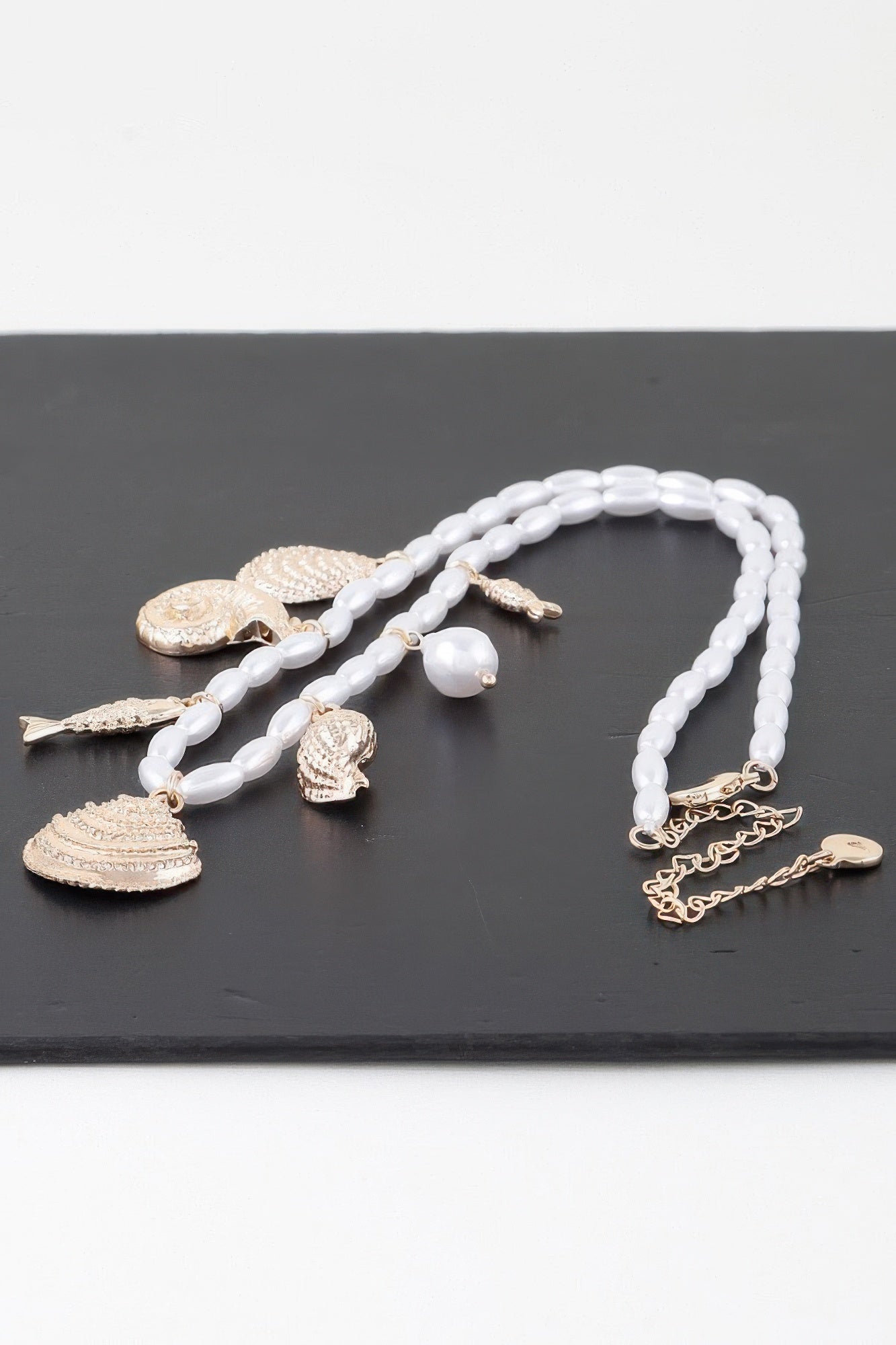 Under The Sea charm necklace laid flat: white beads with gold fish, shell, and star pendants