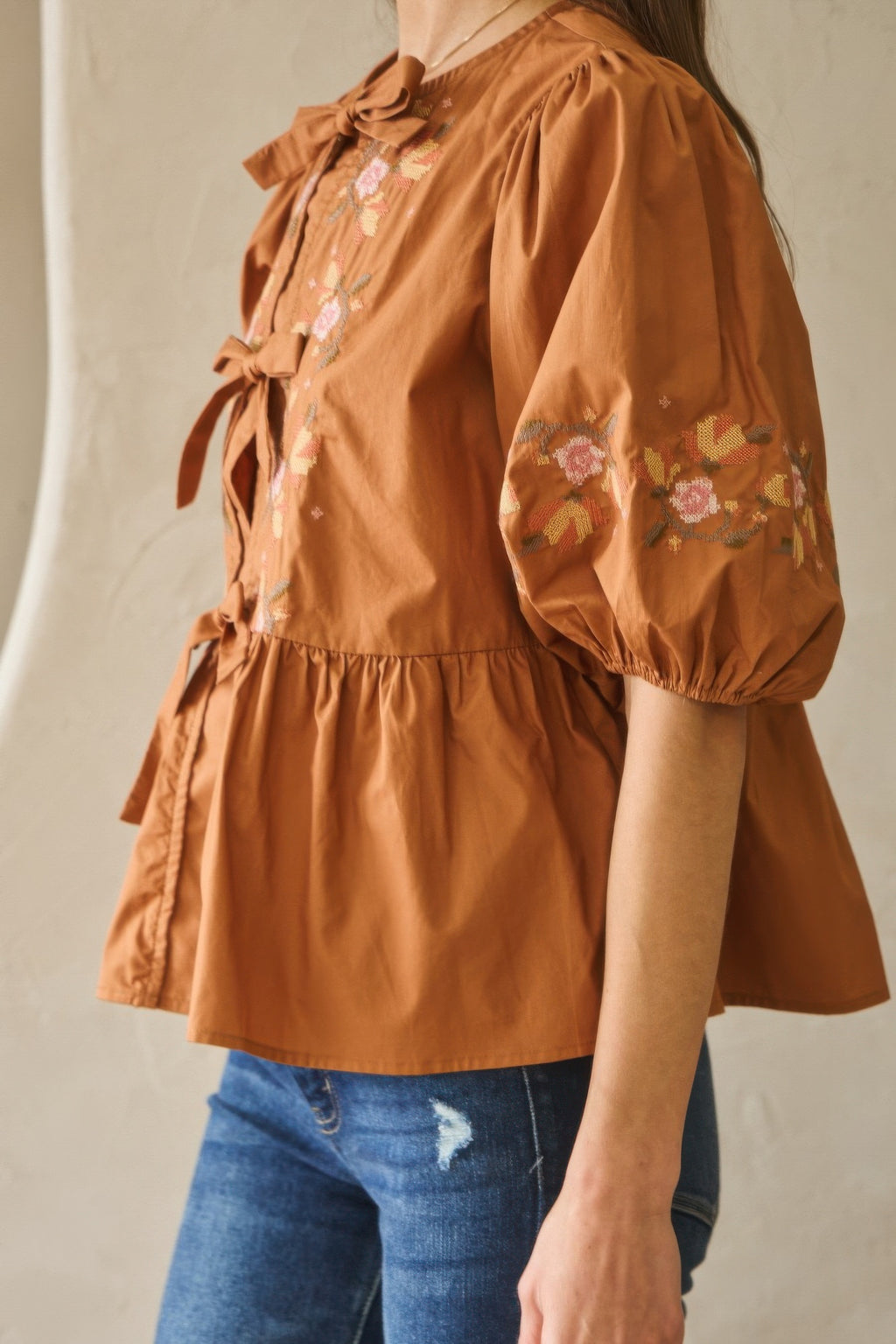 Side view of chesnutt brown poplin blouse with tied bow at neckline and floral sleeves