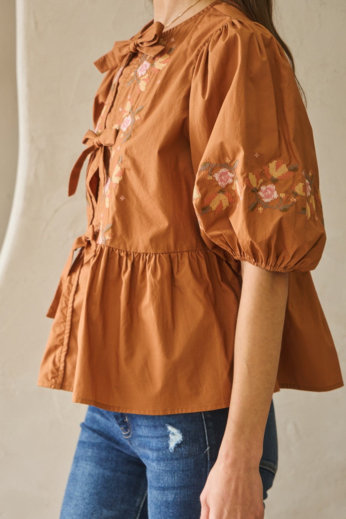 Side view of chesnutt brown poplin blouse with tied bow at neckline and floral sleeves