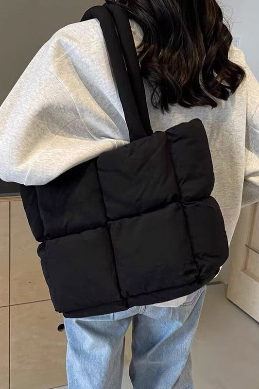 Black quilted puffer convertible tote bag worn with side strap and padded front panel
