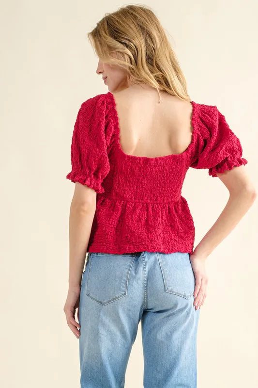 Back view of red textured smocked top with square open back and puff sleeves