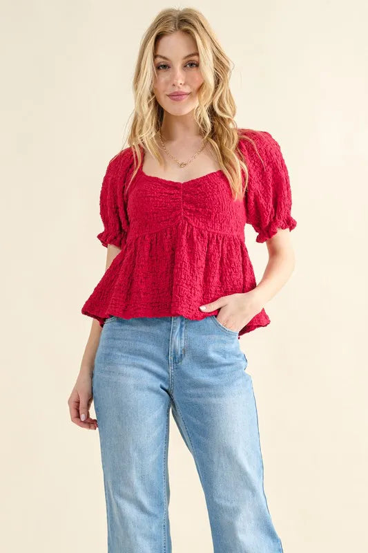 Red textured peplum top with smocked bodice, short puff sleeves, and peplum hem