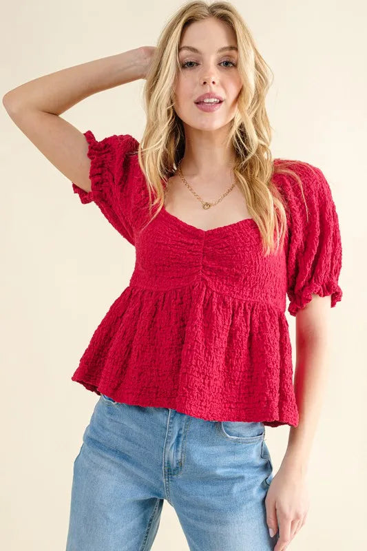 Red textured peplum top with smocked waist, V-stitched neckline, and gathered sleeves
