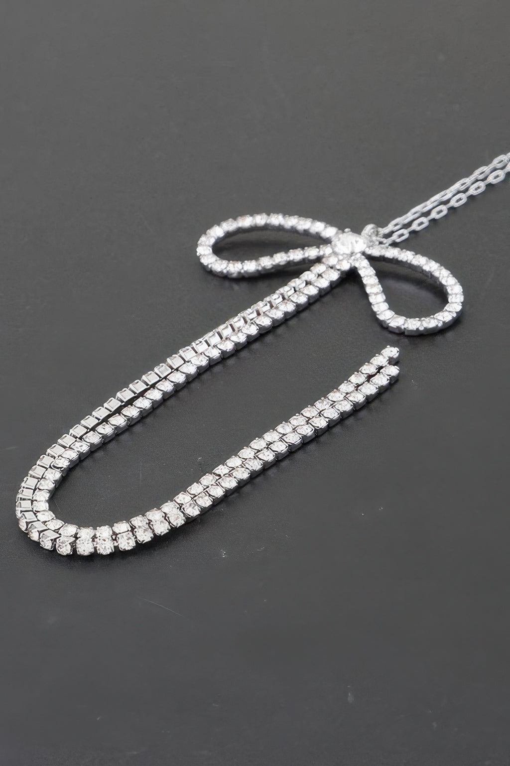 Close-up: clear rhinestone bow detail with sparkling chain links.