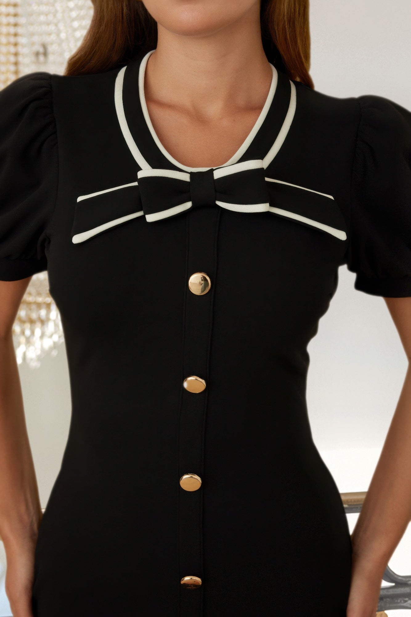 Close-up: ribbon bow collar on black button-up dress with white trim and gold buttons