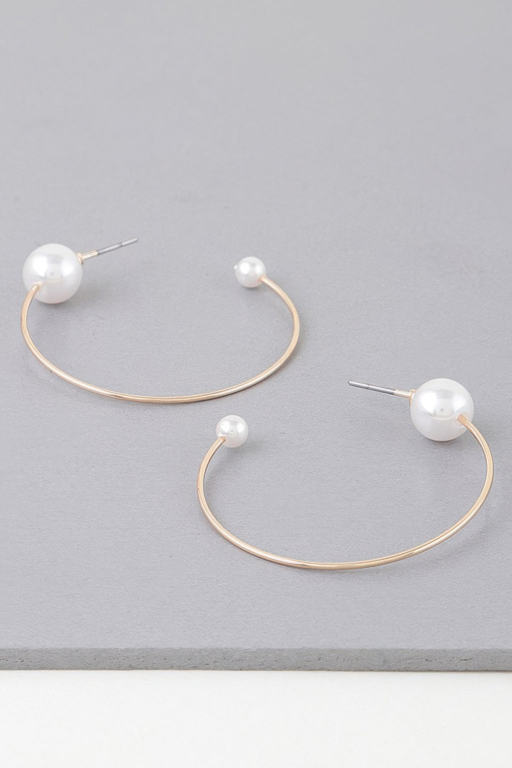Shiny pearl hoop earrings with gold-toned curved wire and white pearl stud ends