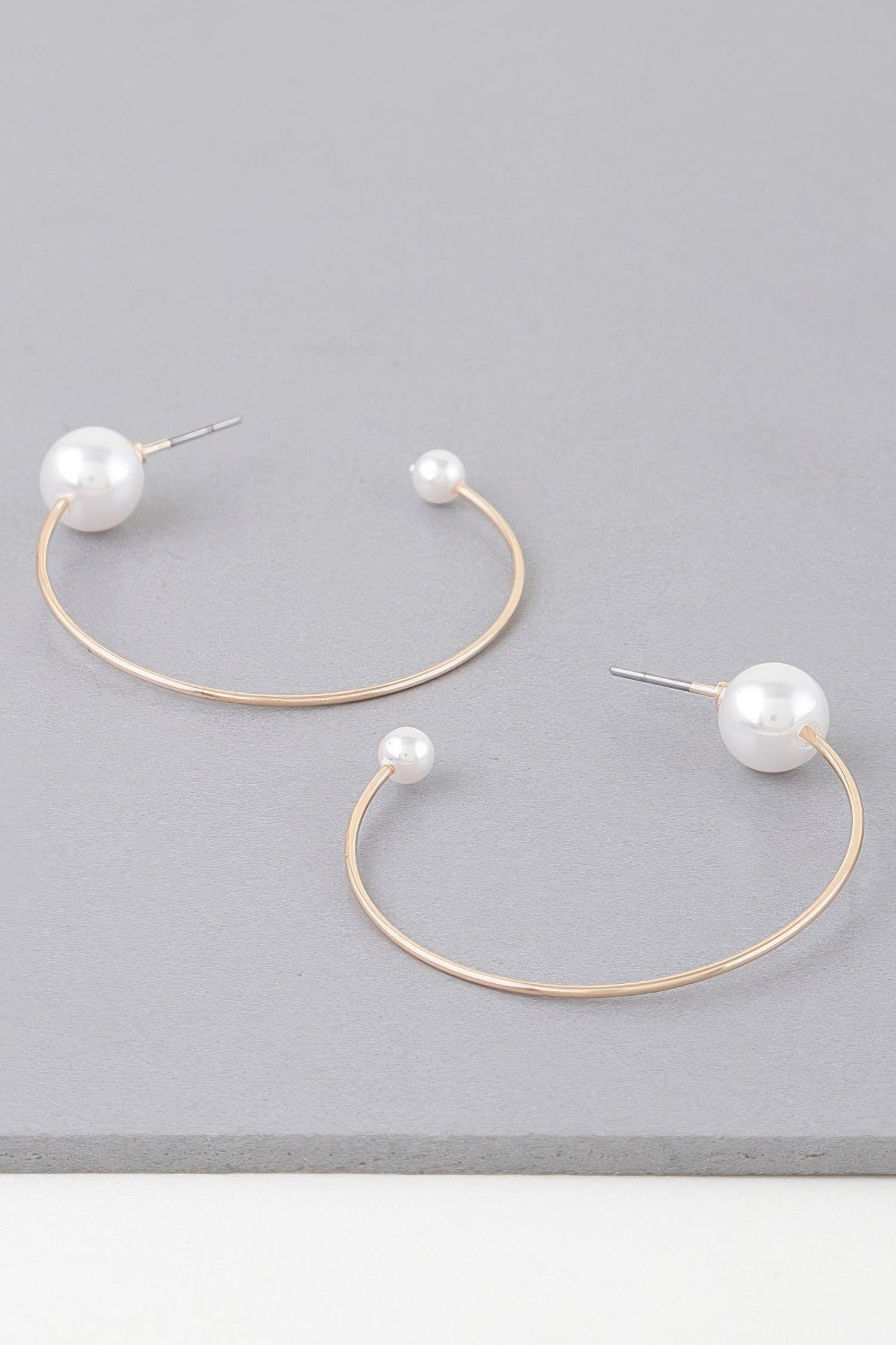 Shiny pearl hoop earrings with gold-toned curved wire and white pearl stud ends
