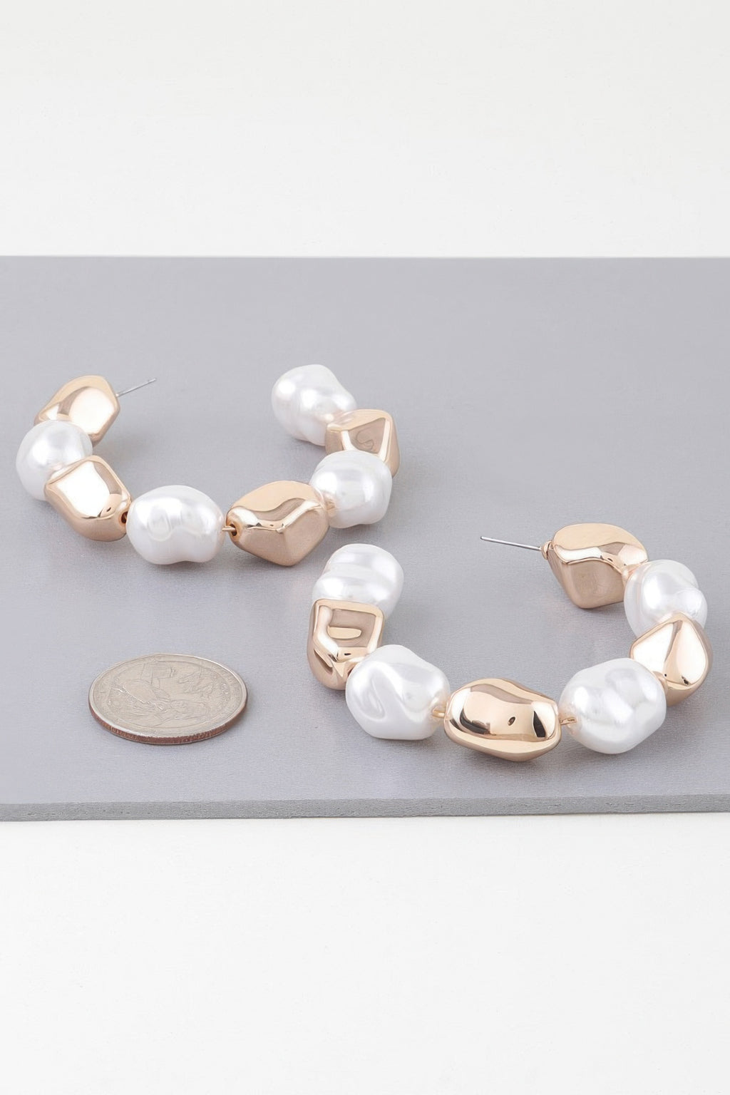 Gold-tone hoop earrings with white pearl beads and hinged clasp, side view