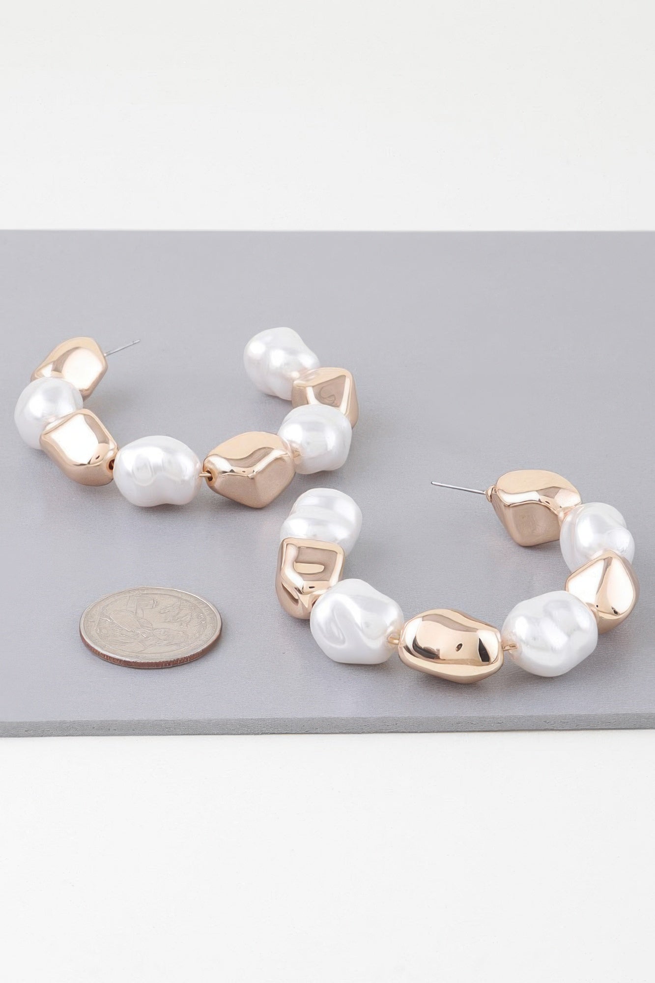 Gold-tone hoop earrings with white pearl beads and hinged clasp, side view